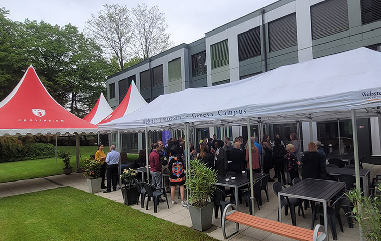 Tents outside the Webster Geneva building with attendees grouped together, talking